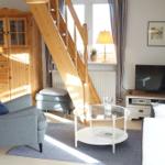 Wohnzimmer mit Sitzgruppe, Glas-Tisch und Holztreppe. Fernseher, Schrank und Fenster sichtbar.