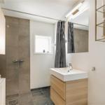 Bad mit Dusche, Waschbecken und Spiegel. Holzmöbel und goldene Regale.