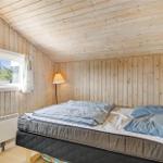 Schlafzimmer mit Holzwand, Bett, Fenster und Stehlampe.