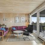 Wohnzimmer mit Holzwand, zwei Sofa, Tisch und Sessel. Durchgang zur Terrasse mit Blick auf Grünflächen.