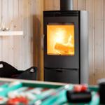 Kaminofen mit brennendem Holz, Holzwand und Tisch im Vordergrund.