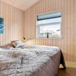 Schlafzimmer mit Holzwandverkleidung, Bett und Fenster mit Blick nach draußen.