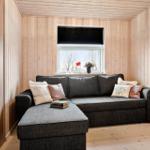 Ein Wohnzimmer mit einem grauen Sofa, Holzwänden und einem Fenster mit Blick auf Bäume.