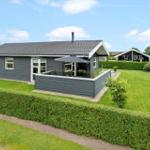 Ein graues Ferienhaus mit Terrasse und Garten. Hinterhof mit Hecke und Grillplatz.