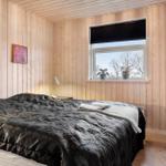 Schlafzimmer mit Holzwänden, Bett mit dunkler Bettwäsche und Fenster mit Blick auf Bäume.