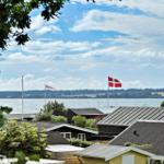 Panorama mit See, Flaggen und Häusern unter blauem Himmel mit weißen Wolken.
