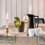 Tisch mit zwei Kerzen, Kaffeekanne und Tassen auf Holzoberfläche.