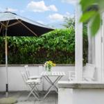 Terrasse mit Tisch, Stühlen und Sonnenschirm. Hintergrund: grüner Heckenzaun.