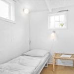 Ein Schlafzimmer mit Bett, zwei Fenstern und einem Hocker.