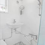 Badezimmer mit Waschbecken, Dusche und Toilette. Bodenfliesen und Fenster sichtbar.