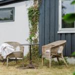 Zwei Rattan-Stühle und ein Tisch stehen im Garten vor einem Haus mit dunklem Holz und weißer Wand.