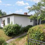 Ein weißes Haus mit Garten, Fenstern und einem Schornstein. Umgeben von Bäumen und Sträuchern.
