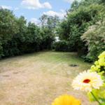 Grüner Garten mit Blumen und Bäumen unter blauem Himmel.