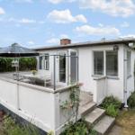 Weiße Villa mit Terrasse, Sonnenschirm und Garten. Eingangstür und Fenster sichtbar.