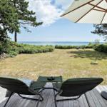 Terrasse mit Liegestühlen und Sonnenschirm. Blick auf Grasfläche und Meer.