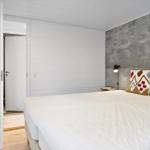 Schlafzimmer mit Bett, Kopfkissen und Bettkopfteil an Betonwand.