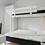 Zimmer mit Doppelstockbett, Schreibtisch und Stuhl. Weiße Wände und Holzboden.