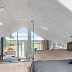 Schlafzimmer mit Blick auf den Strand und Terrasse. Holzboden, Glasgeländer und Dachschräge.