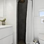 Badezimmer mit Dusche, Waschbecken und Toilette. Weiße Wände und goldener Wasserhahn.