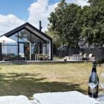 Moderne Villa mit großem Garten und Terrasse. Im Vordergrund stehen ein Weinglas und eine Flasche.