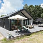 Moderne Villa mit großem Holzdeck, Liegestühlen und Tisch unter freiem Himmel.