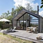 Moderne Hütte mit großem Holzterrasse, Sitzgelegenheiten und Blick auf die Landschaft.