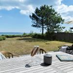 Terrasse mit Tisch, Stühlen und Sonnenschirm. Blick auf Grasfläche und Meer.
