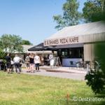 Kaffee- und Pizza-Stand mit Außenterrasse und Gästen unter Sonnenschein.