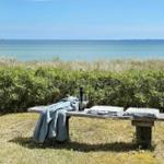 Holzbank mit Decke und Getränk vor Strand und Gras.