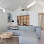 Wohnzimmer mit grauem Sofa, Holzregal und Fernseher. Holzfußboden und weiß gestrichene Wände.