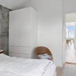 Schlafzimmer mit weißem Bett, Kleiderschrank und Stuhl. Durchgang zur Terrasse mit Blick aufs Meer.