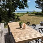 Holztisch mit Stühlen auf Terrasse, Blick auf Grasfläche und Meer.