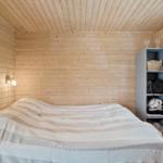 Schlafzimmer mit Holzwand, Bett und Regal. Fenster und Wandlampen sichtbar.