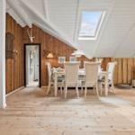 Dining area with white table and chairs under skylight. Wooden walls and floor. TV on stand.