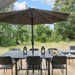 Terrasse mit Tisch, Stühlen und Sonnenschirm. Hintergrund: Grasfläche und Bäume.