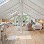 Wohnraum mit Holzfußboden, weißen Möbeln und Kamin. Dachfenster und Glastüren bieten viel Licht.