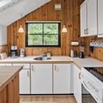 Küche mit Holzwänden, weißen Schränken und Fensterblick auf Bäume.