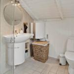 Badezimmer mit Dusche, Waschbecken und Toilette. Weiße Wände und Bodenfliesen.