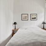 Schlafzimmer mit weiß verkleideten Wänden, Bett, zwei Nachttischen und Fenster.