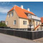 Haus mit rotem Dach, weißen Fenstern und Balkon. Umzäunt mit dunklem Holzzaun.