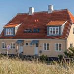 Ein zweistöckiges Haus mit rotem Dach und weißen Fenstern steht unter blauem Himmel.