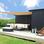 Terrasse mit Sitzgruppe, Sonnensegel und Liegestuhl vor schwarzem Holzhaus.