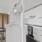 Küche mit Arbeitsplatte, Spüle und Kochfeld. Im Hintergrund Wohnbereich mit Sofa und Tür.