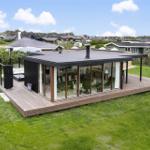 Moderne Villa mit großem Holzdeck und Glasfassade. Grünfläche und Blick auf Wohnhäuser.