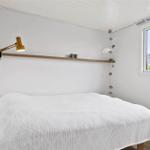 Schlafzimmer mit weißem Bett, Holzregal und Fenster. Decke mit Holzverkleidung.