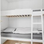 Ein Doppelstockbett mit grauen Matratzen und weißen Kissen in einem Raum mit weiß verkleideten Wänden.