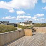 Holzterrasse mit Blick auf Strandhäuser und Dünen unter blauem Himmel.