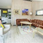 Wohnbereich mit Holzwänden, Sofa, Tisch und Sessel. Küche im Hintergrund sichtbar.