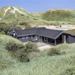 Moderne Hütte mit Terrasse zwischen grünen Dünen und Sandhügeln.