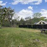 Grüner Garten mit Picknicktisch, umgeben von Wald und Zaun. Ferienhaus im Hintergrund.